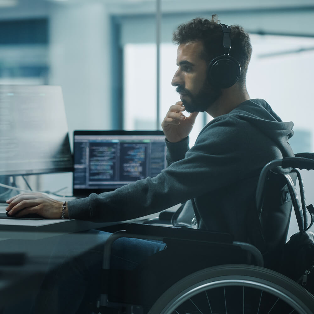 Man in wheelchair sitting behind the desk and looking at the computer monitor