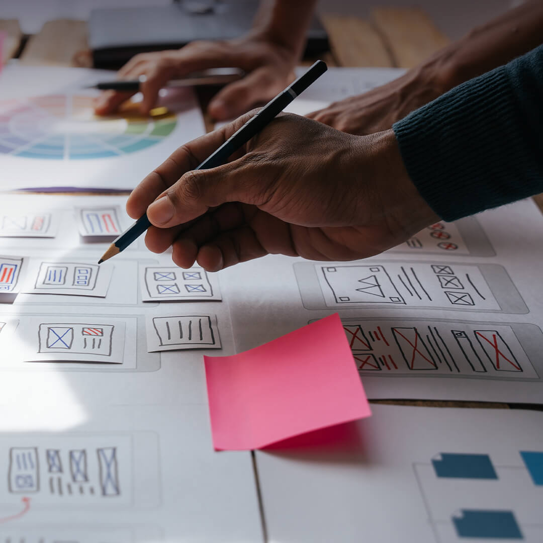 Hands designing a brief with pencil, wireframe sketches, and sticky notes on a desk.